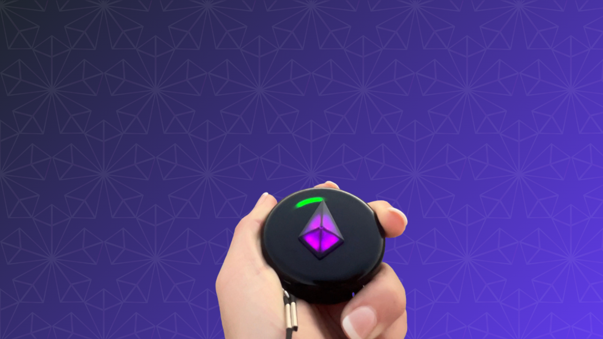 Hand holding a Totem Compass flat with a purple Touch Crystal and a green Bond light on the rim, on a purple patterned background