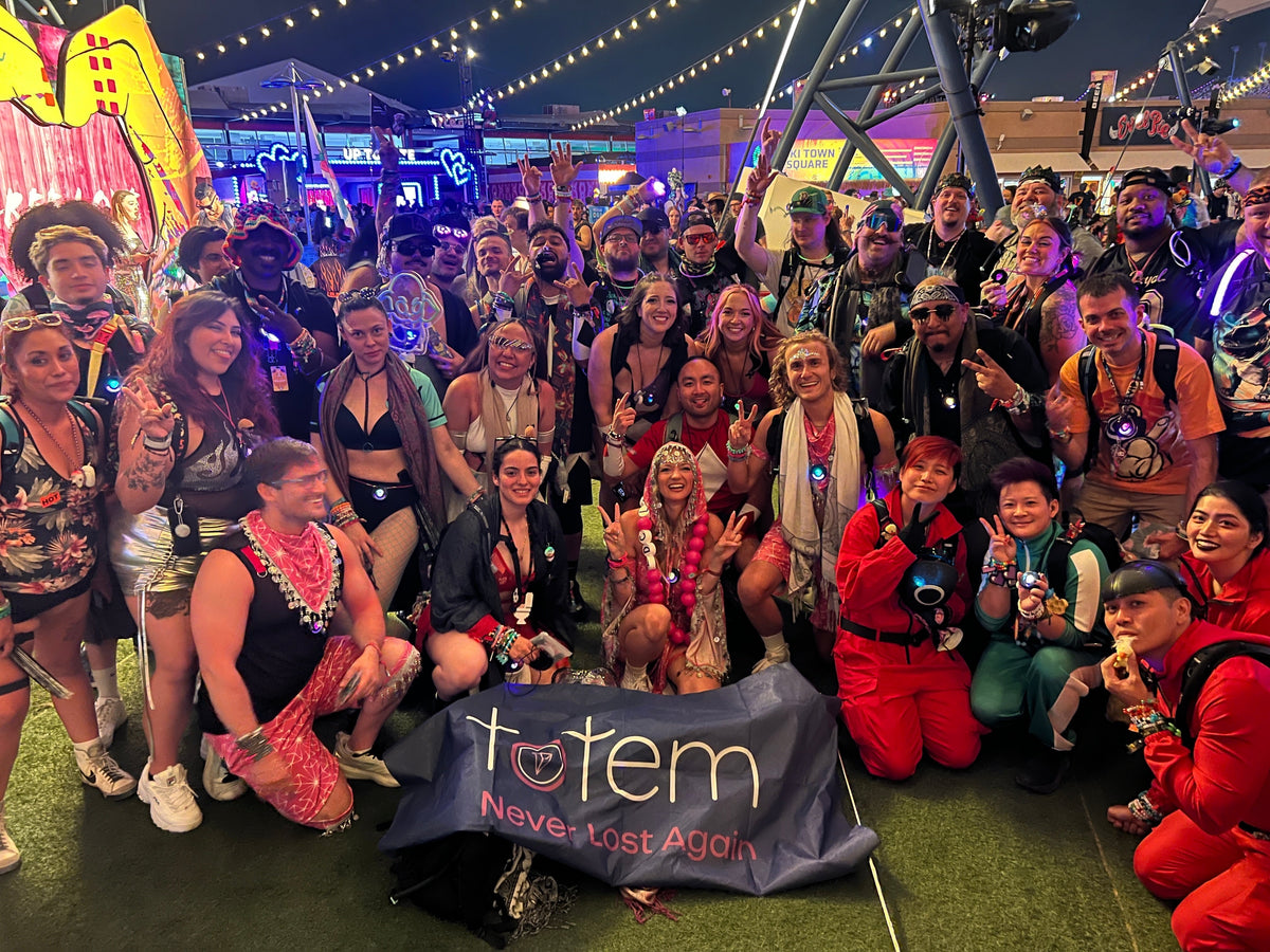 Large group of Totem community members at a night festival meetup, many with glowing necklaces and light-up gear, posing behind a Totem banner