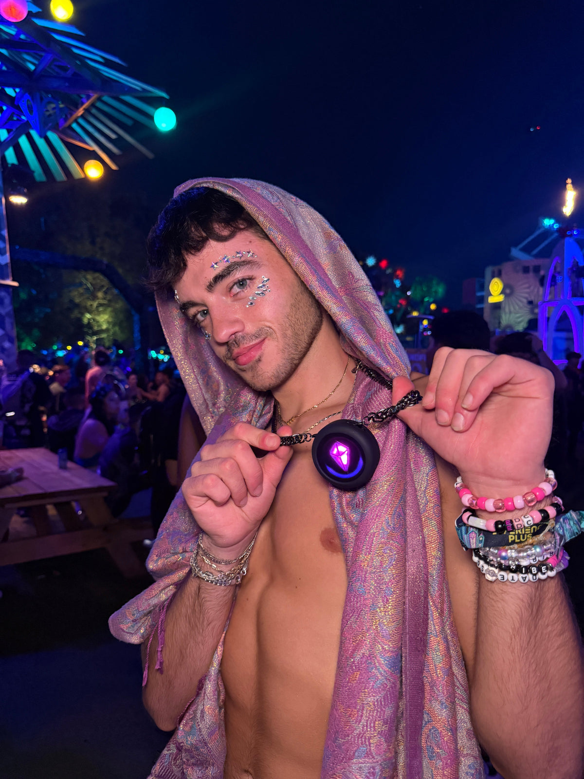 Festival-goer at night holding up a Totem Compass on a chain necklace, its crystal glowing purple