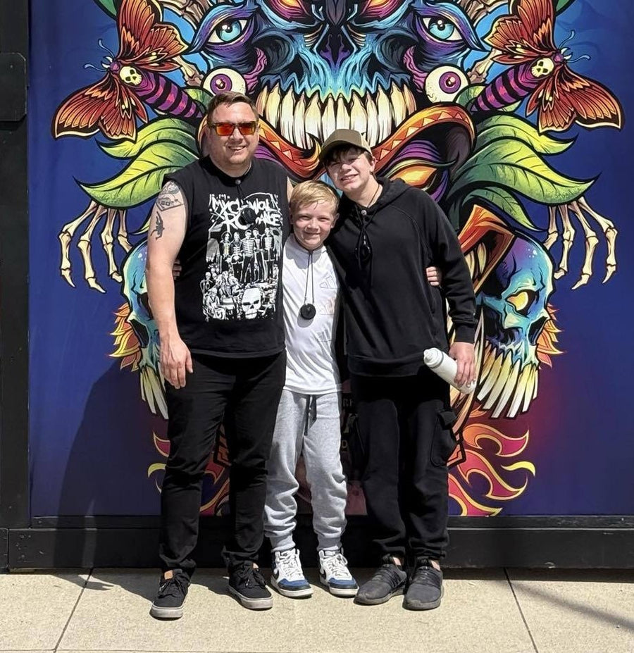 A dad and two kids wearing Totem Compasses in front of a festival mural