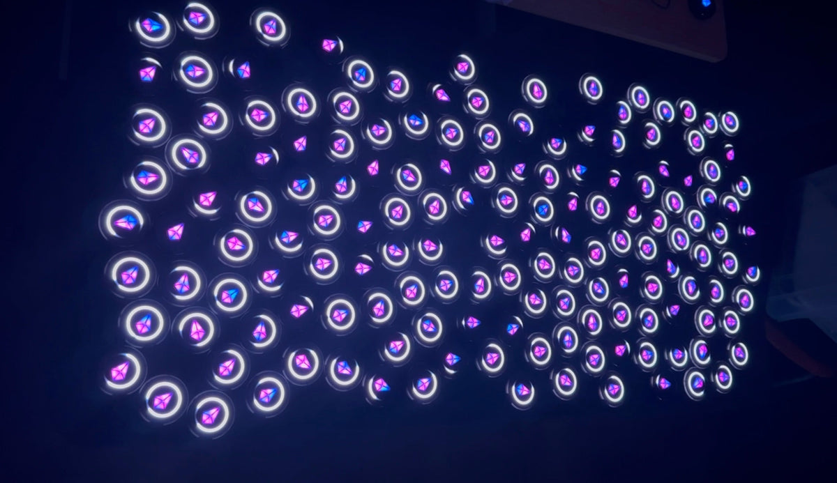 Dozens of Totem Compasses laid out on a dark surface, their rings and Touch Crystals glowing purple, pink and blue