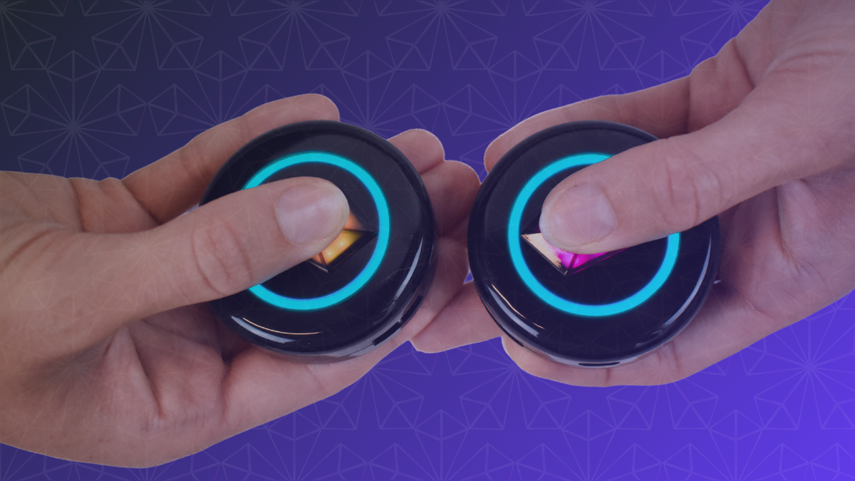 Two hands pressing the Touch Crystals of two Totem Compasses together, both rings glowing blue during Bonding, on a purple patterned background