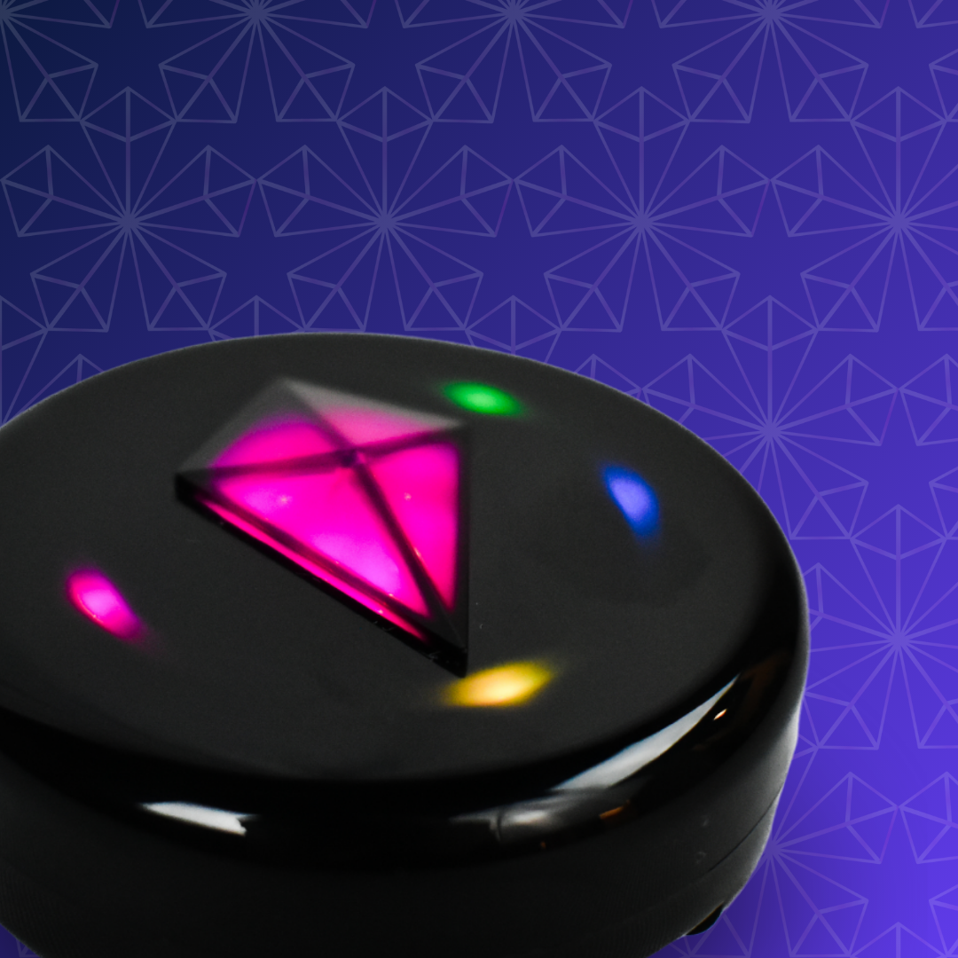 Close-up of a Totem Compass with a glowing pink Touch Crystal and green, blue, yellow and pink Bond Lights around its edge, on a purple patterned background