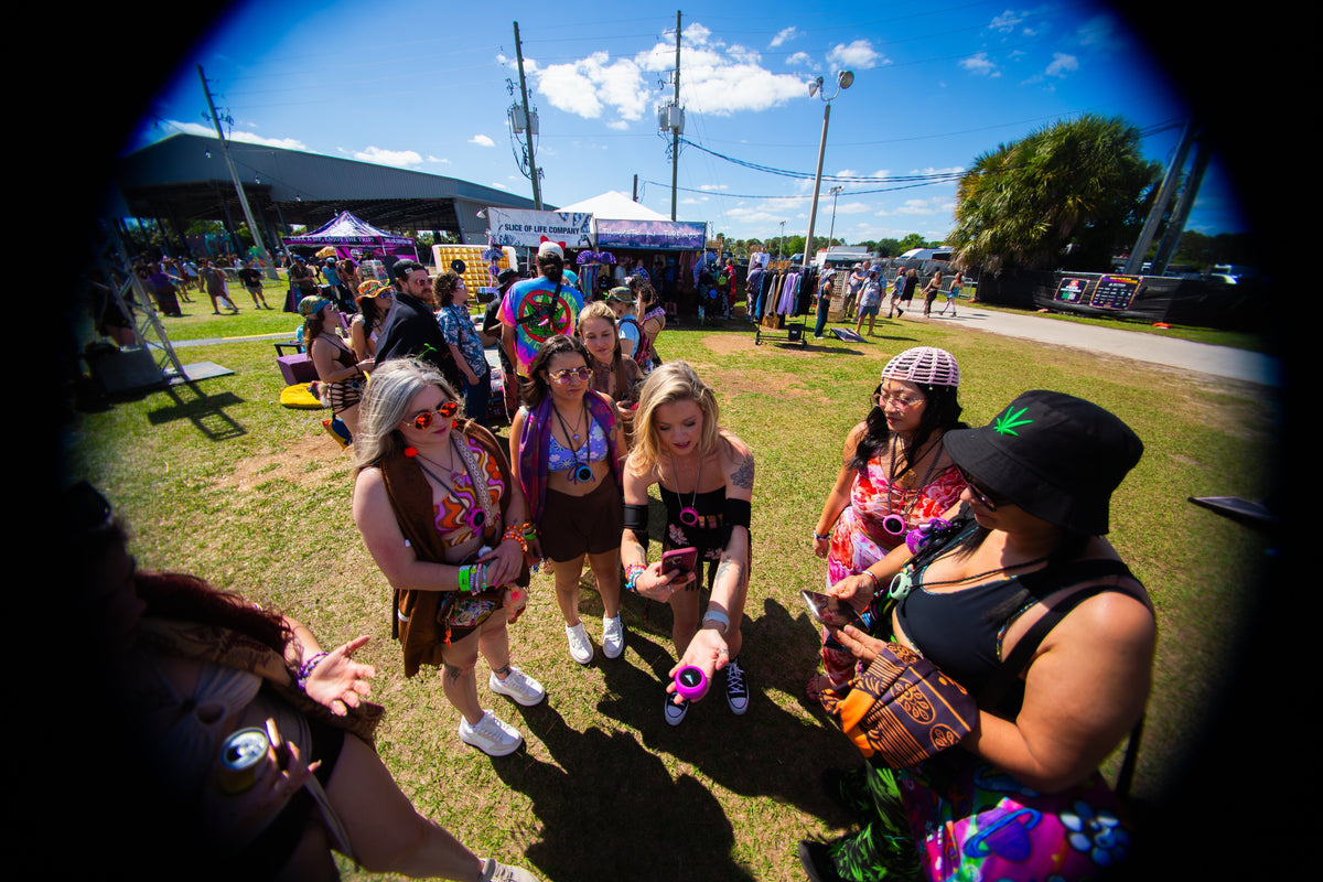 Wide-angle photo of friends at a sunny daytime festival, several holding Totem Compasses and phones